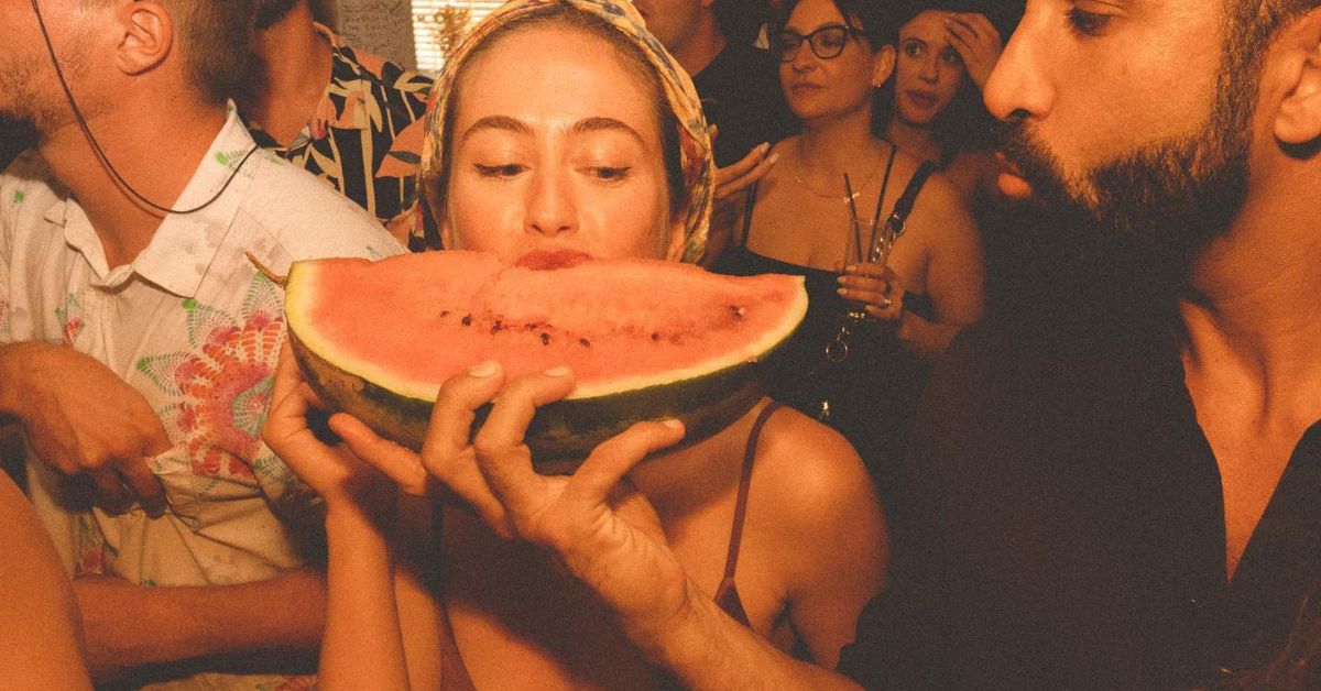 Luxury Mykonos beach club scene with watermelon and champagne in warm sunset lighting